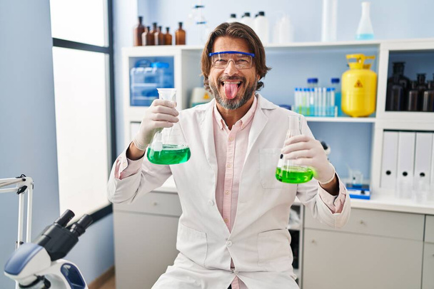 Handsome middle age man working at scientist laboratory doing ok sign with fingers, smiling friendly gesturing excellent symbol  - 写真・画像
