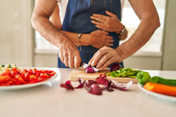 Middle age hispanic couple hugging each other cooking at kitchen - Foto, Bild