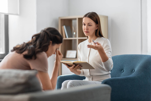 psychology, mental health and people concept - psychologist with notebook talking to stressed woman patient at psychotherapy session - Valokuva, kuva