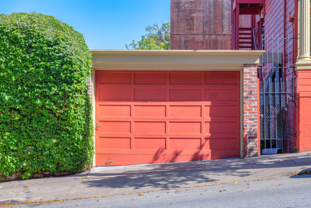 Detached garage exterior with peach wooden garage door at San Francisco, California. There is a shrub wall on the left of the garage and a gate on the right near the red building. - 写真・画像