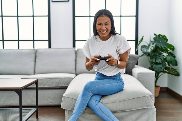 Jovem latina sorrindo confiante jogar videogame em casa - Foto, Imagem