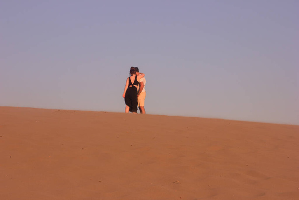Το ρομαντικό ζευγάρι, η πίσω όψη, ένας άνδρας με λευκά ρούχα και μια γυναίκα με ένα μαύρο φόρεμα στέκεται στην άμμο λόφο το ηλιοβασίλεμα, την έννοια της αγάπης, επιλεκτική εστίαση - Φωτογραφία, εικόνα