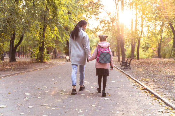 Mom and daughter walk in autumn park. Little girl after school with mother from back. Everyday life - Foto, imagen