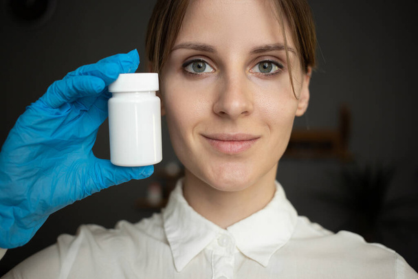 Μια νοσοκόμα που φοράει μπλε ιατρικά γάντια κρατάει ένα μπουκάλι χάπια. - Φωτογραφία, εικόνα