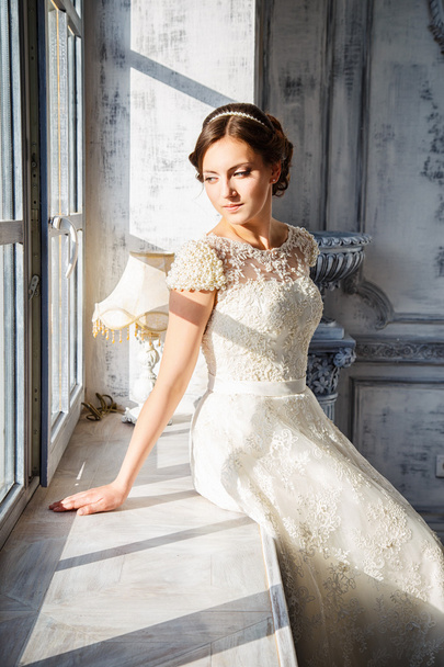 Photo of a beautiful brunette bride in a luxurious wedding dress in elegant expensive interior - Фото, изображение