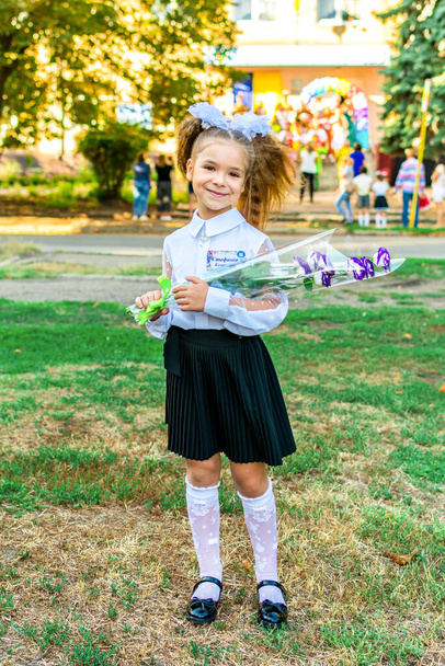 Lysychansk, Ukraine. September 1, 2021 - a girl with a bouquet of flowers in a white blouse with bows on the background of the school during the celebration of the first of September - Foto, Imagen