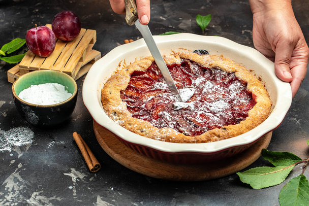 Homemade plum pie. A woman cuts a plum cake with a knife, Food recipe background. Close up, - Zdjęcie, obraz