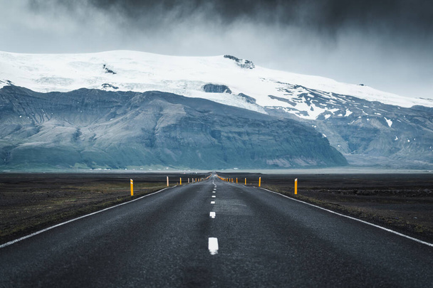 Dramatic straight asphalt road with storm over mountain on gloomy day in Iceland - Photo, image