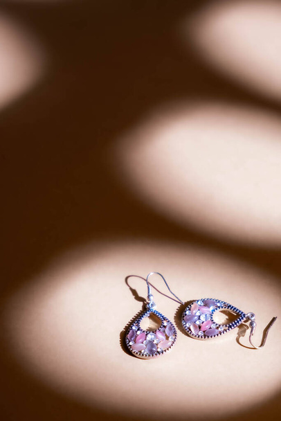 Silver earrings with diamonds on soft brown background. Still life and creative photo with shadows. - Fotoğraf, Görsel