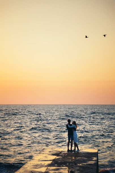 Silhueta de casal em pé no cais, observando o nascer do sol na hora de verão da praia. - Foto, Imagem