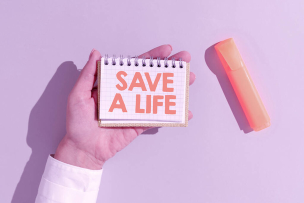 Text caption presenting Save A Life, Business idea Help assistance saving someone from a medical problem or injury Woman Holding Notepad With Important Message On Office Desk With Marker. - Foto, imagen