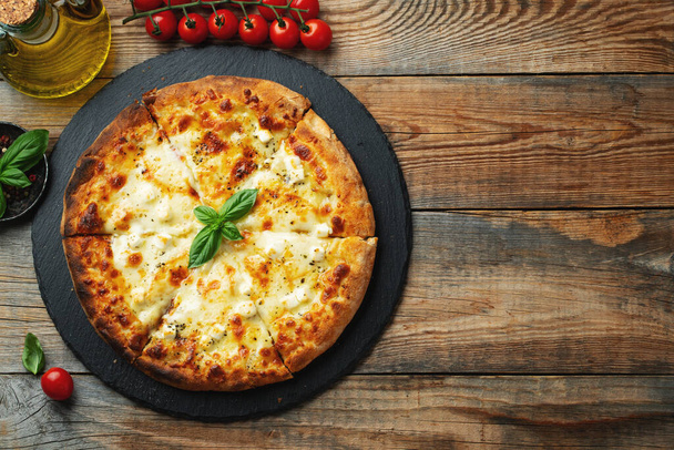 A slice of hot Italian pizza with stretching cheese. Pizza four cheeses with basil on a wooden background. Top view with copy space. - Valokuva, kuva