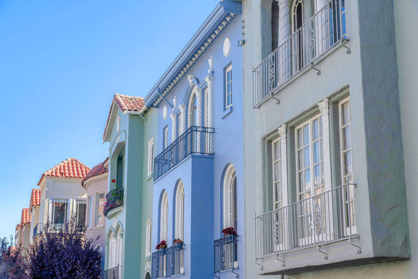 Покрашенный ряд домов с оконными перилами на фасаде в Сан-Франциско, Калифорния. Слева дерево с фиолетовыми листьями рядом с домами справа со средиземноморским внешним видом. - Фото, изображение