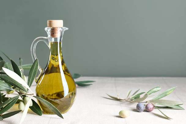 Aceite de oliva virgen extra y rama de olivo en la botella sobre la mesa con mantel de lino. Alimento mediterráneo saludable. - Foto, Imagen