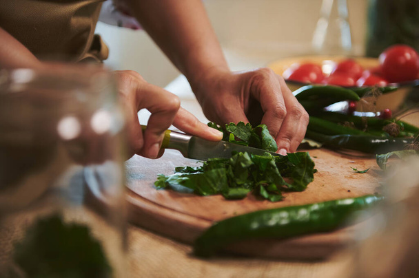 Detail: Hands of a housewife in beige chefs apron chopping fresh fragrant culinary herbs on a wooden cutting board while preparing a pickle marinade for pickling chili in the kitchen. homemade food - Fotoğraf, Görsel