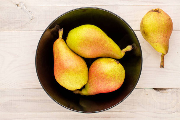 Four juicy pears with a black ceramic plate on a wooden table, close-up, top view. - 写真・画像