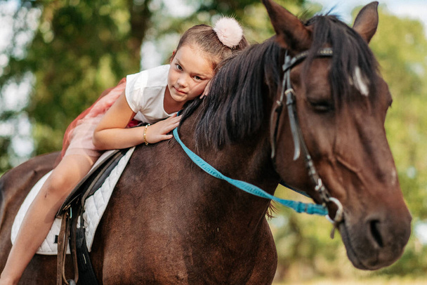 The girl lies on a horse and hugs her. Rehabilitation of a child through contact with a horse. Friendship of a girl and a horse. - Photo, image