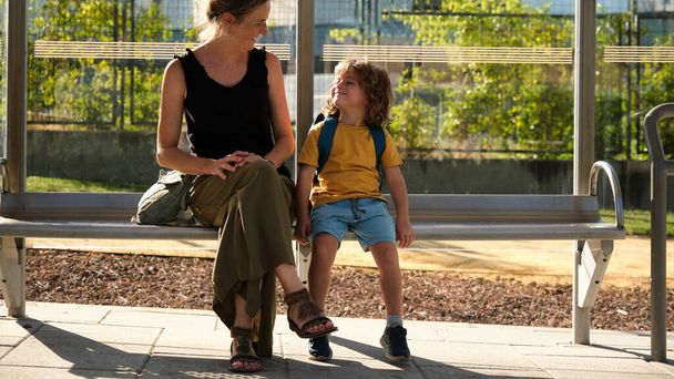 Mother and toddler wait for bus at bus stop to go to school - Foto, Bild
