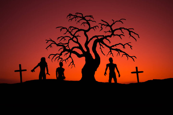 Gün batımında mezarlıkta yürüyen zombileri siluetle. Ürkütücü yüzlü korkunç Cadılar Bayramı ağacı silueti. Korku Cadılar Bayramı konsepti. Seçici odak - Fotoğraf, Görsel
