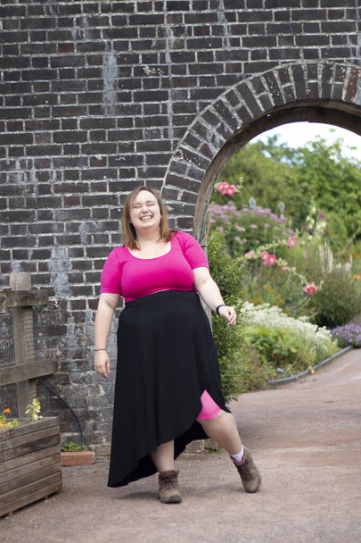 Plus size woman wearing pink and walking around in front of an arch way on a travel adventure - Foto, imagen