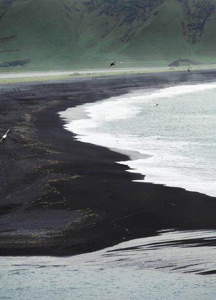 A vertical shot of the beautiful Black Sand Beach in Iceland with water washing the shore - Фото, зображення