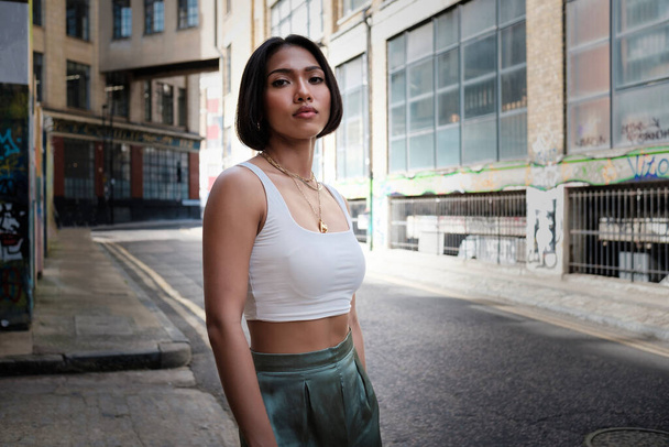 Portrait of asian female standing in a narrow London street looking at camera. White sleeveless t-shirt. - Foto, Imagen