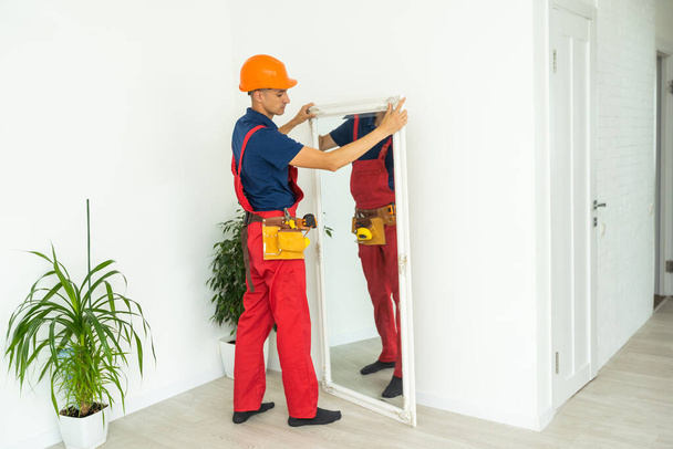 Сборка мебели. ремонтник устанавливает зеркало в гостиной нового дома - Фото, изображение