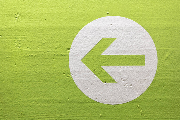 An arrow on a white circle isolated on a green wall showing the direction - Foto, Imagem
