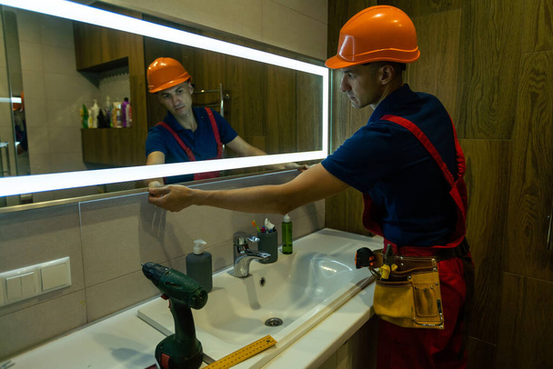 O trabalhador instala o espelho no banheiro - Foto, Imagem