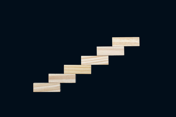 Wooden details lined up in the form of steps on a black background. Wooden rectangles form the shape of the steps. The concept of career growth or rise from the bottom up - Foto, Imagen