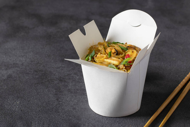 Noodles with seafood and vegetables in takeaway box on dark gray table - Foto, Imagen