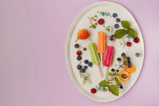 Bright colorful popsicles on a white tray with berries on a light violet background with copy space. Banner with summer ice cream ice pop - Foto, Imagem