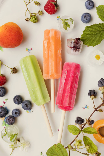 Bright colorful popsicles on a white tray with berries and ice cubes on a light violet background. Tasty ice pops close up - Foto, Imagem