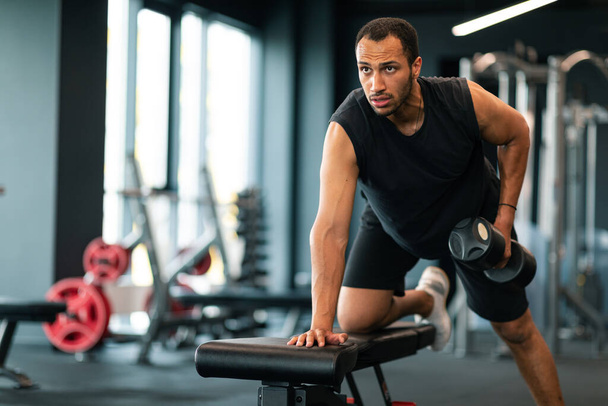 Portrait Of Motivated Black Sportsman Exercising With Dumbbell At Gym, Handsome Muscular Young African American Guy Training With Light Weights In Modern Fitness Club Interior, Copy Space - Photo, image
