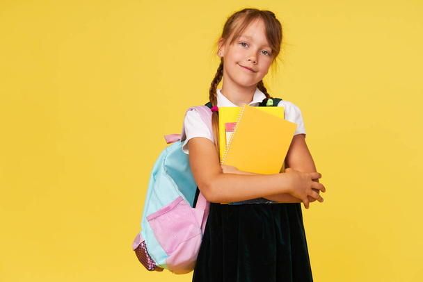 Portrait of a schoolgirl with textbooks and a backpack on a yellow background. Back to school - Foto, afbeelding