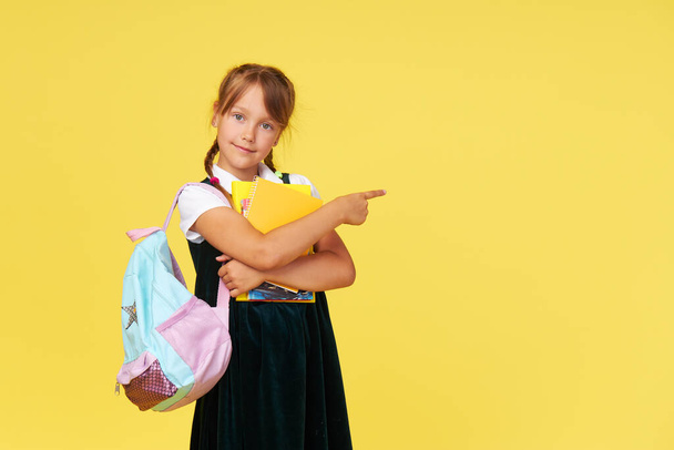 Portrait of a schoolgirl with textbooks and a backpack on a yellow background. Back to school - Фото, изображение