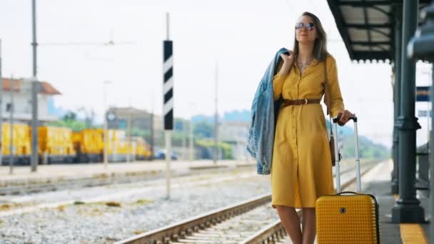 Woman with travel suitcase is waiting for a train. - Séquence, vidéo