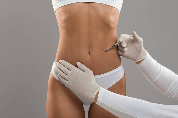 Lipolysis Concept. Young Woman In Underwear Getting Beauty Injection For Slimming, Unrecognizable Beautician Wearing Gloves Making Aesthetic Procedure For Fit Female With Sporty Body, Grey Background - Foto, Bild