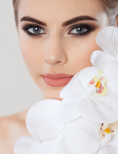 Portrait of a woman with beautiful make-up holds a white orchid in his hand. Professional makeup and skin care. - Zdjęcie, obraz