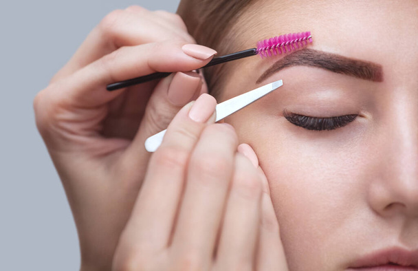 Master makeup corrects, and gives shape to pull out with forceps previously painted with henna eyebrows in a beauty salon. Professional care for face. - Photo, Image