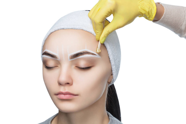 The make-up artist plucks her eyebrows, before the procedure of permanent make-up in the beauty salon. - Photo, Image
