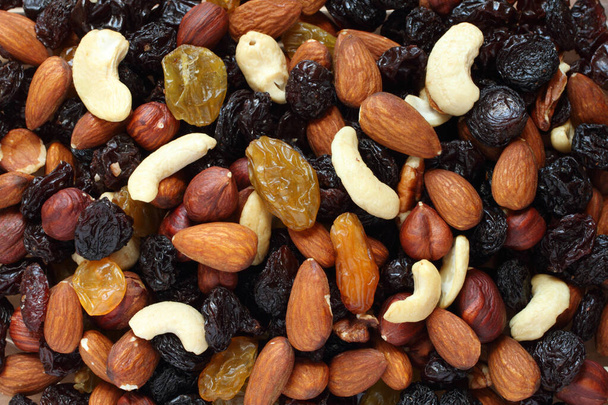 Top view of a pile of large shelled almonds, shelled hazelnuts, cashew nuts, large dark blue raisins and yellow raisins, dried cranberries arranged randomly. Closeup - Valokuva, kuva