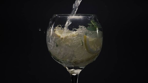 Blubbernder Zitroneneis-Minze-Cocktail in Nahaufnahme. Frischer Wasserstrahl gießt Eiskräuter und Limetten im Weinglas auf. Sprudelnder Limonadenmojito trinkt schwarze Sicht. Leckeres Getränk mit Tropfen. Cocktail-Konzept erstellen - Foto, Bild