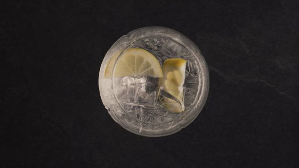 Hände werfen Minze in Zitroneneis. Zutaten im Glas mit kaltem Aqua auf schwarzer Marmoroberfläche. Kaltes Getränk an der Bar von oben. Konzept für sommerliche Detox-Cocktails - Foto, Bild
