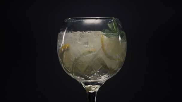 Fizzy cytrynowy lód miętowy bąbelkowy koktajl zbliżenie. Woda gazowana witaminami z kroplami i kostkami lodu w kieliszku do wina super slow motion. Makro widok czarne tło powierzchni. Koncepcja letnich świeżych napojów zimnych - Zdjęcie, obraz