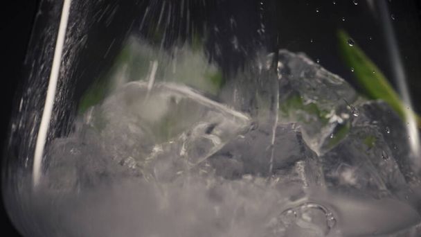 Kaltes Minzgetränk in Weinglas-Nahaufnahme. Sparkling Soda Wasserstrahl mit Tropfen Füllglas mit Kräutern Makroansicht schwarzer Hintergrund. Mojito erfrischendes leckeres kohlensäurehaltiges Cocktailkonzept - Foto, Bild