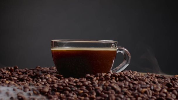 Töltött átlátszó espresso csésze pörkölt kávébab kupac közelről. Bögre forró erős energikus ital áll halom barna friss magok. Koffein ízletes reggeli ital sötét alapon.  - Fotó, kép