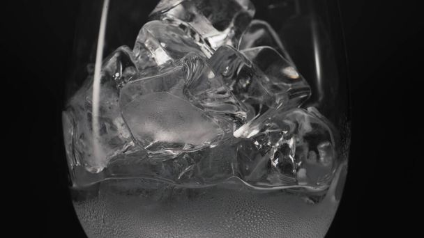 Bloques congelados derritiendo primer plano de la copa de vino. Cubos de hielo llenando vidrio transparente caído con condensación. Bebidas frías y cócteles macro fondo negro. Concepto de calmante de sed - Foto, Imagen