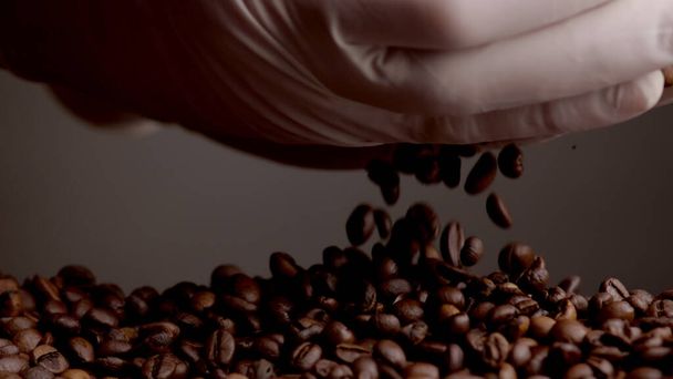 Запечене насіння кави виливає руки в рукавички крупним планом супер повільний рух. Невідома людина бере свіжі коричневі зерна в долоні. Перевірка якості кавових зерен. Ідеальний ароматичний інгредієнт для ранкового напою
. - Фото, зображення