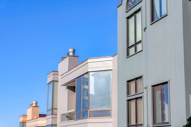 Ряд будинків з балконами, картинними вікнами і флюїнами проти неба в Сан-Франциско, Каліфорнія. Є сірий будинок справа з панелями вікна біля будинків з рефлективними вікнами.. - Фото, зображення